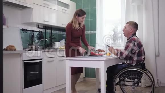 幸福的夫妻幸福的男人坐在轮椅上和一个微笑的妻子在厨房准备食物视频的预览图