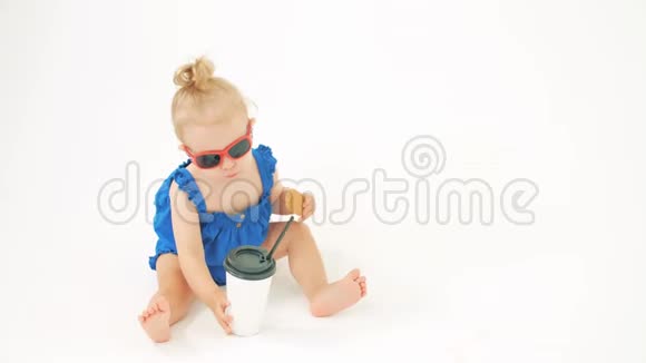酷酷的女婴戴着太阳镜在白色背景下用吸管从纸杯里喝饮料视频的预览图