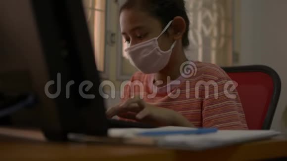可爱的女孩戴着防护面具在COVID19疫情爆发期间在家里的办公桌上工作和写作视频的预览图