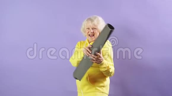 穿着黄色运动衫的时髦奶奶拿着瑜伽垫走向音乐视频的预览图