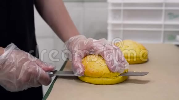 一个戴手套的人把一个带着芝麻的面包切成两半上面的特写是一把刀视频的预览图