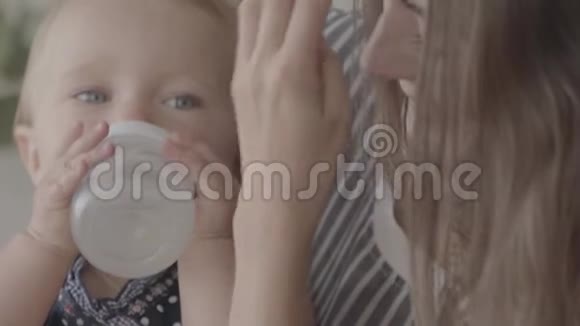 特写可爱的年轻女人从厨房里的小婴儿瓶里喂她的女婴幸福家庭的概念视频的预览图