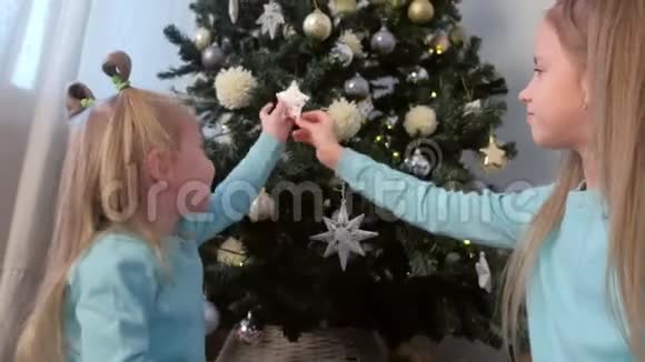 两个女孩姐妹用玩具雪花和星星装饰圣诞树视频的预览图