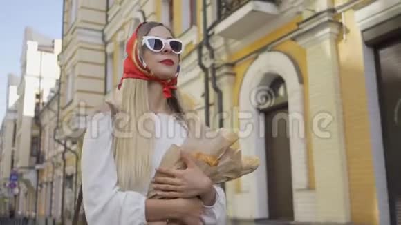 积极美丽的年轻女子走在街上拿着刚烤好的面包和羊角面包时尚迷人视频的预览图