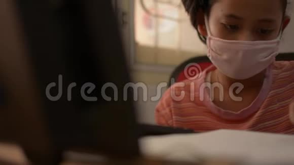 可爱的女孩戴着防护面具在COVID19疫情爆发期间在家里用电脑写字视频的预览图