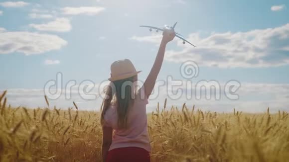 可爱的女孩在日落时在麦田里玩玩具飞机儿童玩玩具飞机的剪影视频的预览图