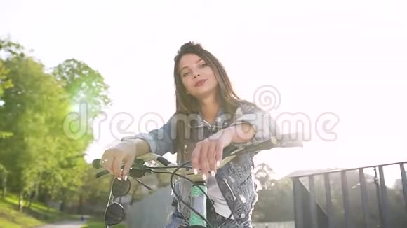 时髦开朗的性感女人棕色长发坐在自行车上看着相机阳光明媚的日子戴着太阳镜视频的预览图