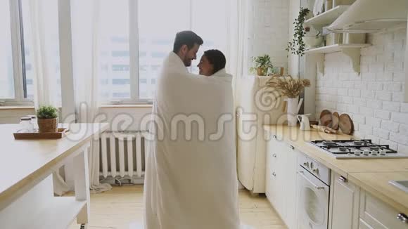 幸福浪漫的年轻夫妇站在厨房里裹着毯子视频的预览图