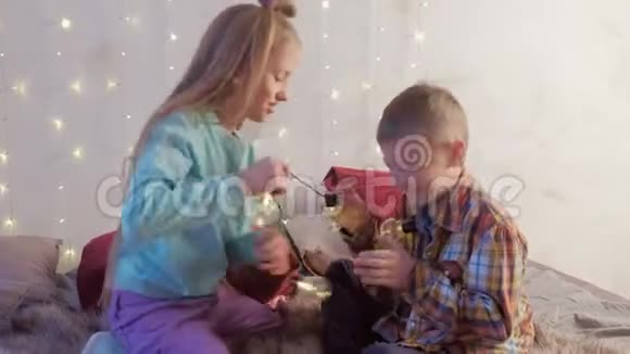 男孩和女孩的朋友玩花环坐在床上在圣诞节的内部视频的预览图