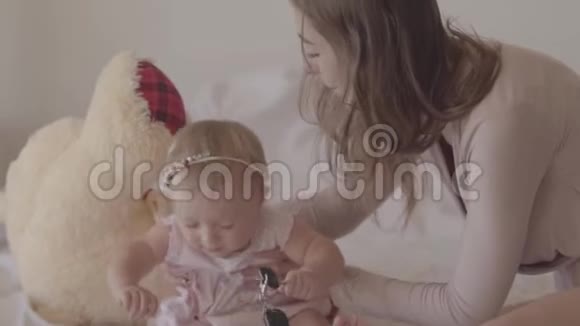 年轻的女人和一个坐在床上的小女婴玩耍做母亲的乐趣在家爱家人美丽美丽视频的预览图