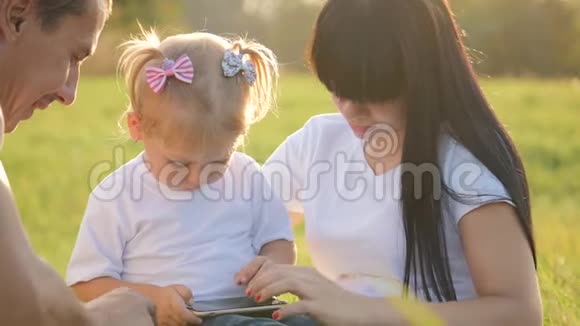 一个幸福的家庭花时间在户外爸爸妈妈和他们的金发小女儿坐在草地上快乐的孩子视频的预览图