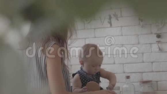 可爱的妈妈和她的宝贝女儿在厨房准备食物那孩子一边玩谷物罐子一边玩视频的预览图