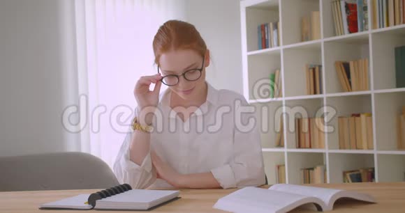 年轻漂亮的红头发女学生修着眼镜看着镜头开心地坐着视频的预览图