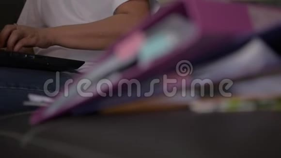 穿着休闲装的女人坐在一个带手提电脑和一堆文件的皮革沙发上视频的预览图
