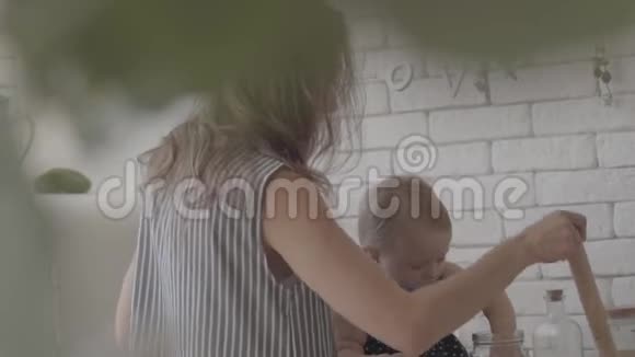 年轻的母亲和她的宝贝女儿在厨房准备食物那个女人在玩她的孩子给她看擀面杖视频的预览图
