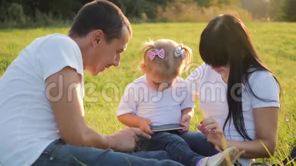 一个幸福的家庭花时间在户外爸爸妈妈和他们的金发小女儿坐在草地上快乐的孩子视频的预览图