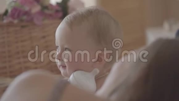 漂亮的女婴坐在妈妈家附近的床上玩瓶子可爱的白种人在室内视频的预览图