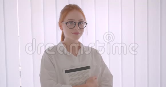 年轻漂亮红头发的女学生戴着眼镜拿着一本书看着站在镜头前的镜头视频的预览图