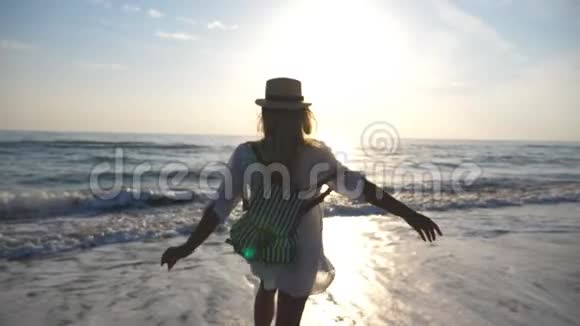 年轻快乐的女人穿着衬衫背着背包跑到海里日出时用脚喷水漂亮姑娘视频的预览图