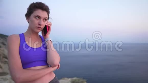 年轻成功的商务女性在一座悬崖上训练时穿着运动上衣和紧身裤的年轻女性会接电话视频的预览图