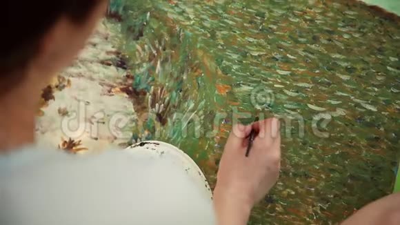 一个女人用画笔在画布上画用印象派风格的小笔画特写镜头从后面俯视视频的预览图