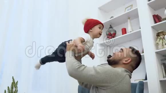 英俊可爱的父亲抱着他可爱的婴儿在房间的空气中装饰精美的圣诞树视频的预览图