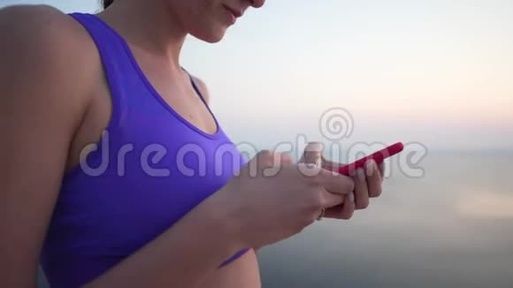一个穿胸罩的小女孩手里拿着一部手机在外面做网上购物在锻炼时特写视频的预览图