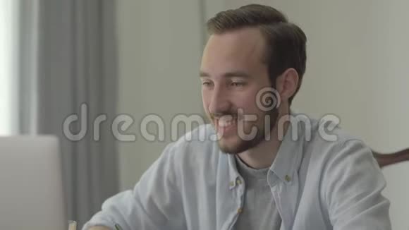 一个年轻英俊的男人坐在办公室的电脑前微笑点头的肖像上班族视频的预览图