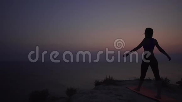 一位身材苗条的年轻女子在日落时练习瑜伽的剪影举起她的手臂冥想体式和团结视频的预览图