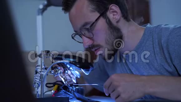 一个年轻的留着胡子的人戴着眼镜在他的工作场所用烙铁工作的概念视频的预览图