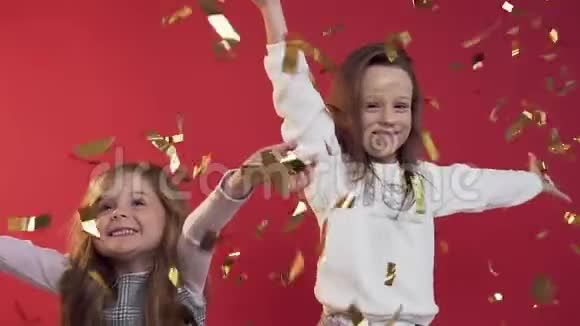 漂亮小女孩在红色背景上投掷金色五彩纸屑的慢动作视频的预览图