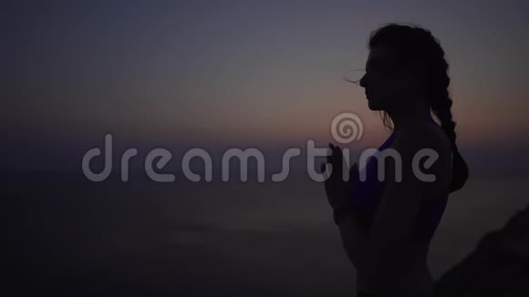 平静和女孩练习瑜伽在日落时在海边在悬崖上冥想运动的女人像在视频的预览图