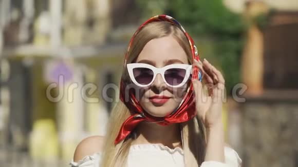戴墨镜的年轻可爱女子在城市街道上戴着红色披肩的镜头视频的预览图