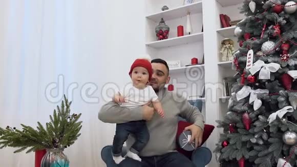 英俊的男人手里拿着有趣的小婴儿给他看漂亮的礼物坐在椅子上靠近视频的预览图