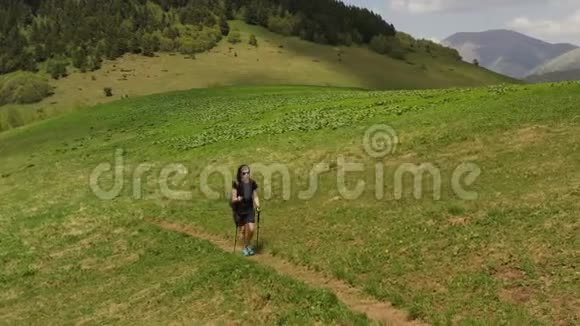 用长途跋涉的杆子戴太阳镜的女孩走在绿色的山坡上视频的预览图