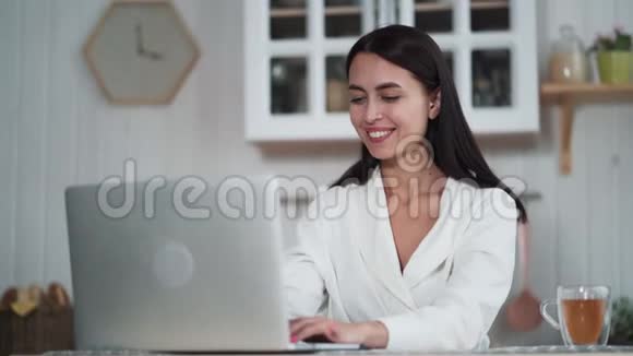 年轻的微笑女性自由职业者早上在家里用笔记本电脑工作视频的预览图