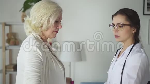 穿着白色制服的漂亮医生正在帮助老年妇女正确地锻炼身体视频的预览图