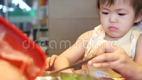 一个亚洲小女孩帮她妈妈把烹饪材料放进沸腾的火锅里视频的预览图
