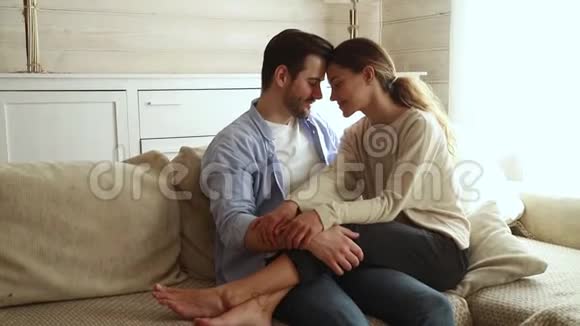 浪漫幸福的年轻夫妇抚摸着额头笑着拥抱在沙发上视频的预览图