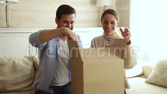 快乐兴奋的情侣顾客打开坐在沙发上的纸板箱视频的预览图