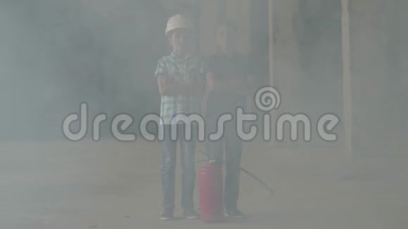 两个戴着白色安全帽的小男孩站在烟雾弥漫的房间里的灭火器旁边火灾易燃性概念视频的预览图