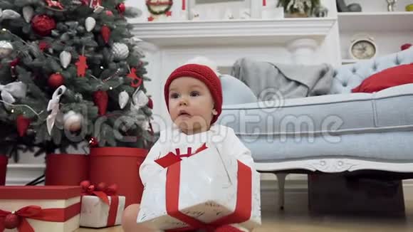 可爱的蹒跚学步的孩子穿着圣诞衣服坐在地板上在圣诞节的背景上送着漂亮的礼物视频的预览图