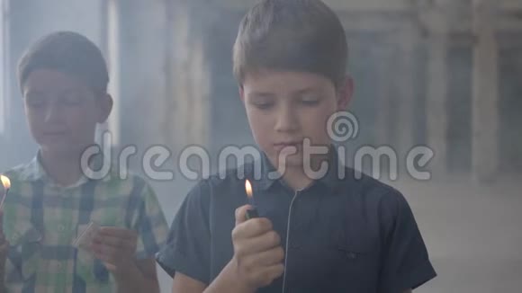 两个可爱的男孩在一个烟雾弥漫的废弃房间里一个男孩拿着燃烧的火柴第二个男孩拿着燃烧的打火机视频的预览图