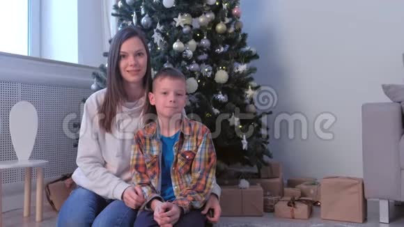 在家中坐在圣诞树旁微笑的母子的家庭画像视频的预览图