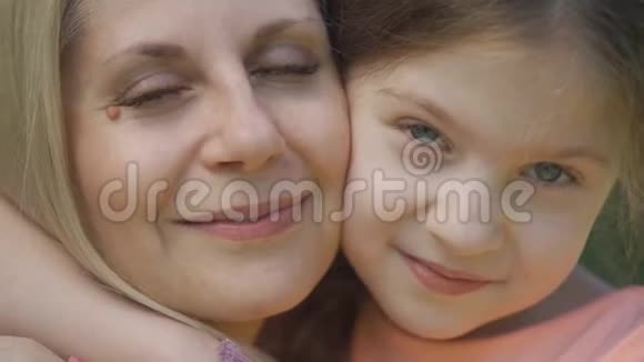 特写照片金发母亲和她的小女儿拥抱在夏季公园看镜头快乐的爱视频的预览图