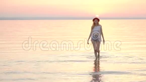 年轻的金发女郎戴着帽子在海上享受暑假金色的夕阳视频的预览图