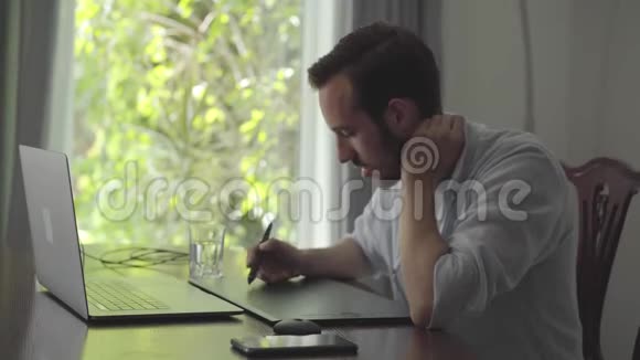 英俊的技术胡子男人画使用图形平板电脑看笔记本电脑男性手绘三维动画制作视频的预览图
