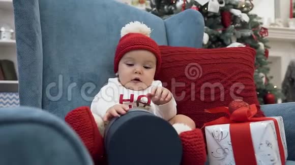 可爱的小女孩在圣诞树旁的舒适扶手椅中享受圣诞礼物视频的预览图
