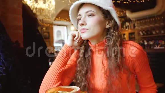 咖啡店里漂亮漂亮的女孩看起来很可爱年轻卷曲的绿眼睛女人戴着时髦的蓬松帽子和橙色视频的预览图
