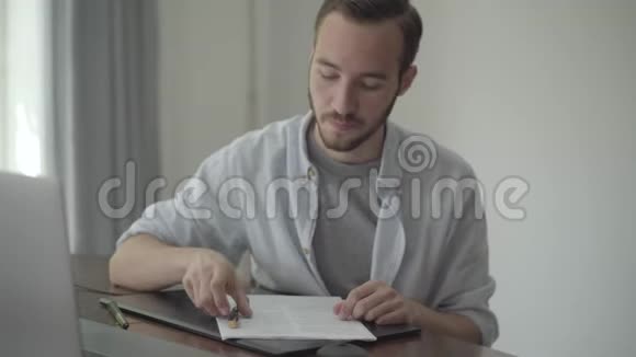 年轻的作家坐在桌子旁用黑色和金色的钢笔批改他在纸上写的文章并竖起大拇指视频的预览图
